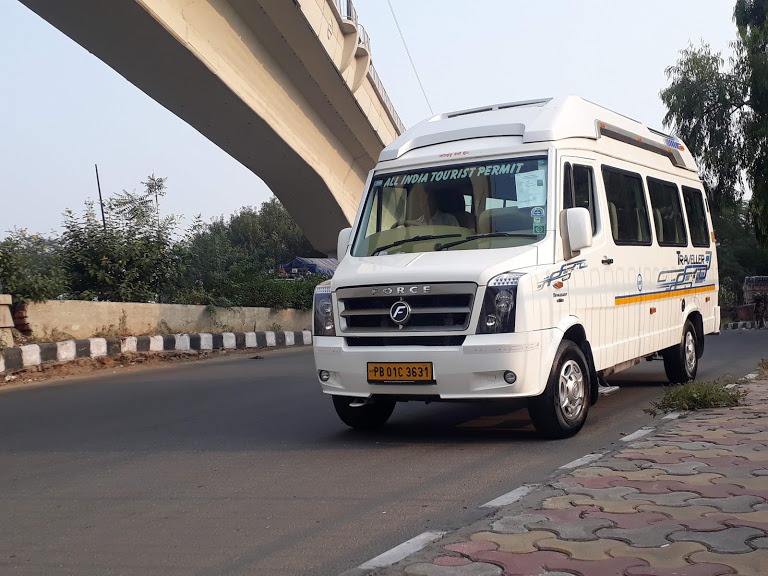 A Tempo Traveller parked along a road under a bridge, showcasing dependable and affordable taxi services in Kolhapur.