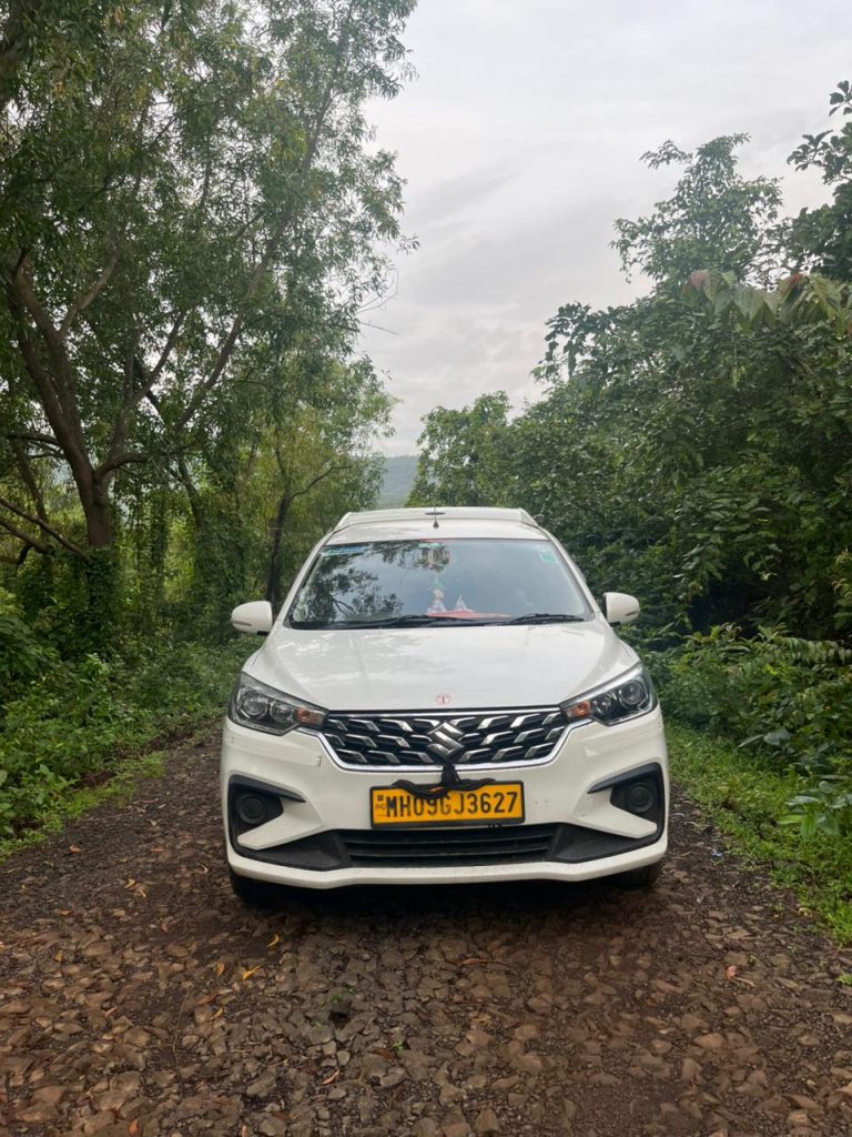 Ertiga cab parked on the hilly road having trees along both sides.